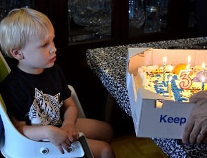 3-year-old boy in high chair looks at a Costco cake with candles 