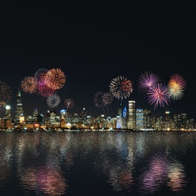 colorful fireworks explode above a city skyline at night; the view is across a body of water