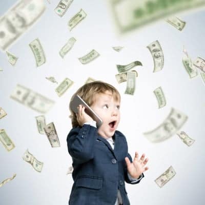 A child wearing a suit and calling on the phone with money flying in the background