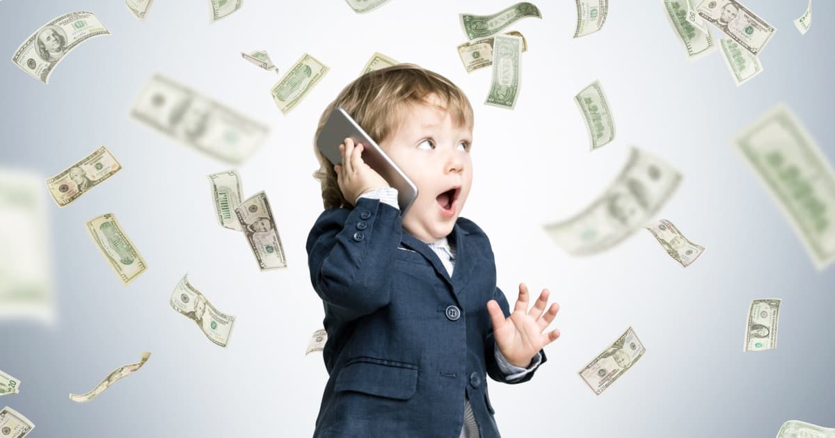 A child wearing a suit  speaking on the phone while money is flying in the background