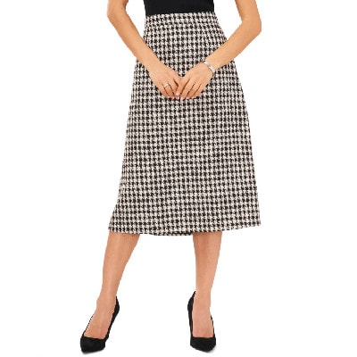 A woman wearing a black top, black heels, and houndstooth-print skirt