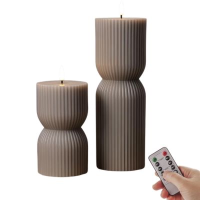 A set of two brown flameless candles next to a person's hand holding the remote