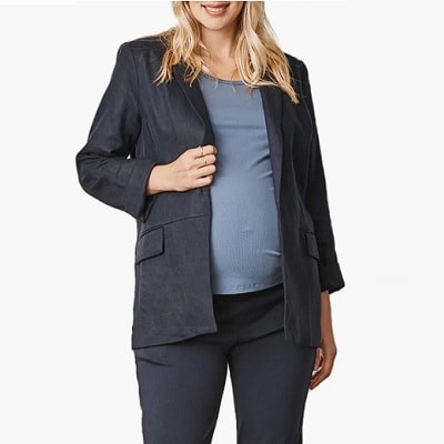 A pregnant woman wearing a light blue top, navy maternity blazer, and navy pants