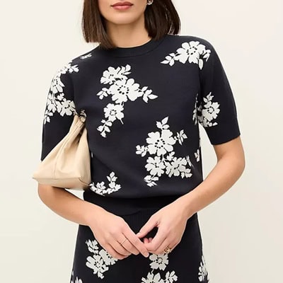 A woman wearing a black-and-white floral top and matching skirt, and carrying a beige bag