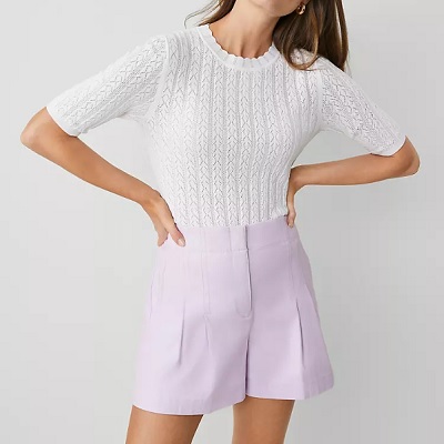 A woman wearing a white pointelle sweater and lavender shorts