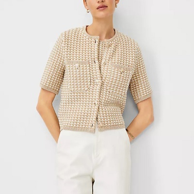 A woman wearing a tan tweed jacket, matching top, and white pants