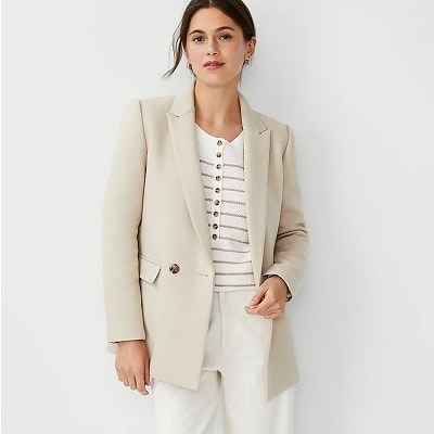 A woman wearing a white striped top, a cream-colored double-breasted blazer, and off-white pants