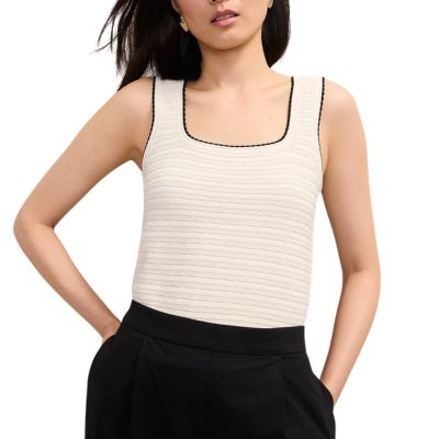 A woman wearing black pants and an off-white sweater shell with black stitching around the neckline and straps