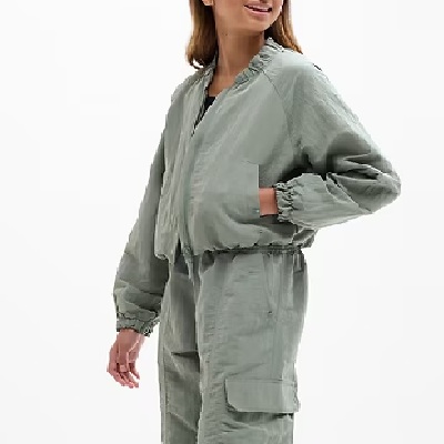 A woman wearing a light green bomber jacket, matching pants, and a black top