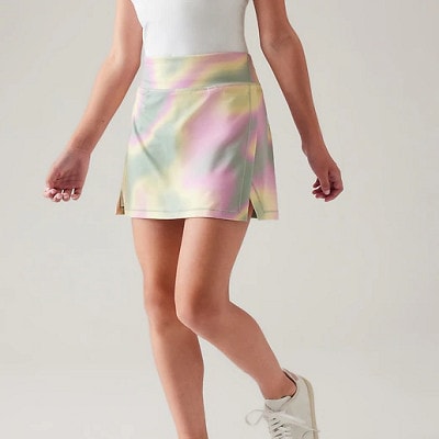 A girl wearing a white top, white sneakers, and a multicolor skort