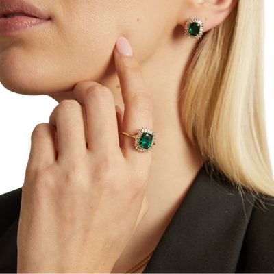 A closeup of a woman's face and hand. She is wearing a black top and matching gold-and-emerald earrings.