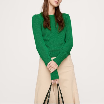 A woman wearing a green knit sweater and beige skirt