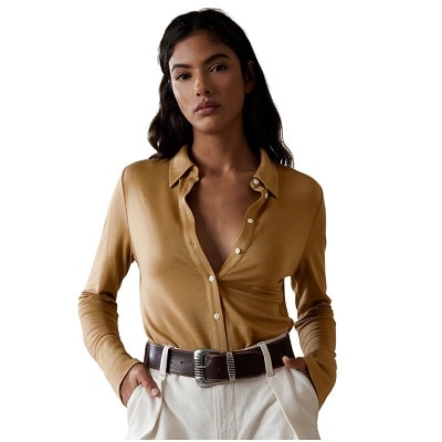 A woman wearing a dark mustard colored button-front shirt, a brown belt, and white pants