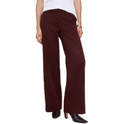 A woman wearing burgundy pants, black boots, white top, and silver bracelet
