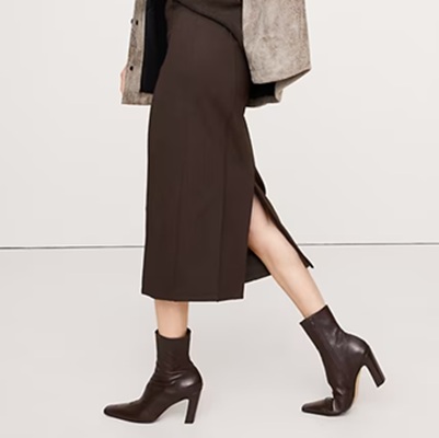A woman wearing a gray jacket, brown midi skirt, and brown heeled boots