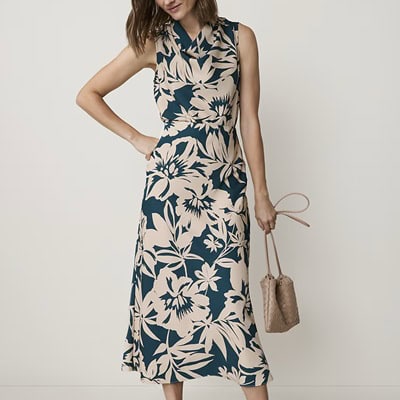 A woman wearing a beige-and-navy floral dress and carrying a brown woven handbag