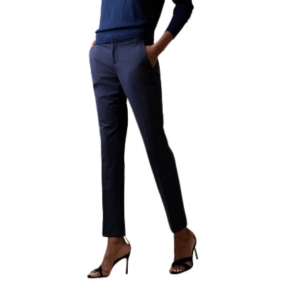 A woman wearing a blue top, blue tailored pants, and heels