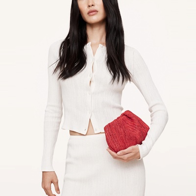 A woman wearing a white top and white skirt, carrying a red clutch