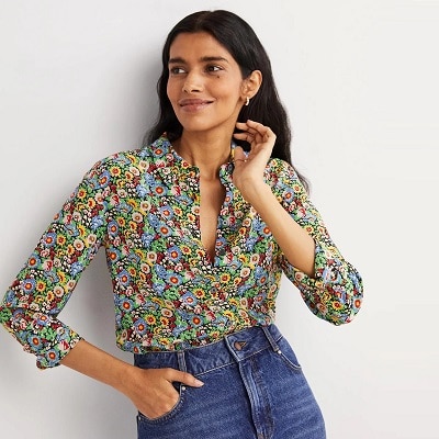 A woman with long black hair wearing a floral print blouse and blue jeans