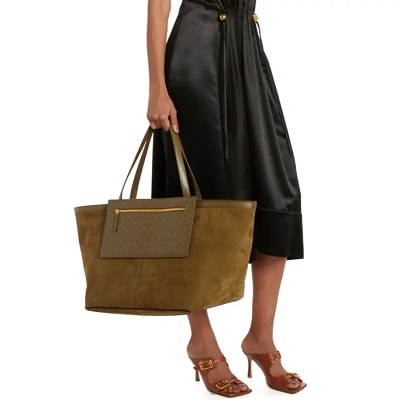 A woman wearing a black skirt, carrying a large, brown suede tote