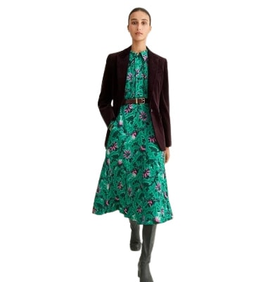 A woman wearing a green floral dress with blazer and boots