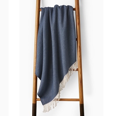 A brown wooden ladder with a blue throw blanket with white fringe hanging on it