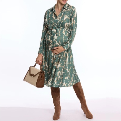 A woman wearing a abstract-print green long sleeve maternity dress and high brown boots with brown handbag