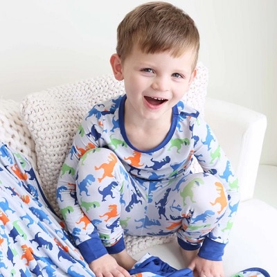 A young boy wearing T-Rex pajamas and sitting next to a matching blanket