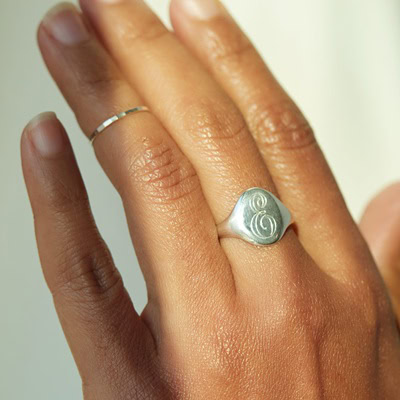 A closeup photo of a woman's hand wearing a silver "E" signet ring and a thin silver band on different fingers