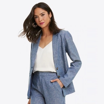 A woman with long black hair wearing a chambray blazer and matching pants with a V-neck white top underneath