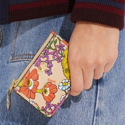 A woman's hand holding a floral card case in front of her denim skirt 
