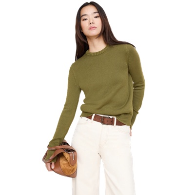 A woman wearing an olive green sweater, white pants, and brown belt, and carrying a brown handbag