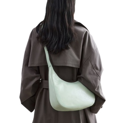 A woman wearing a gray trench coat and carrying a light green handbag