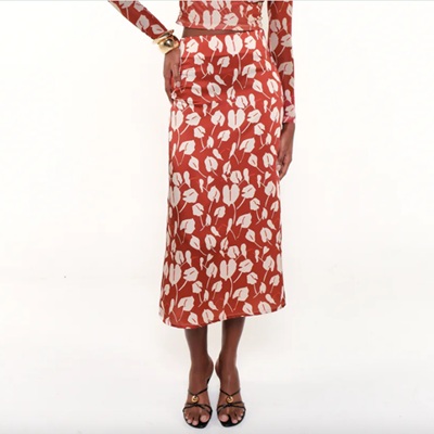 A woman (lower half shown) wearing a red-orange floral dress and black sandals