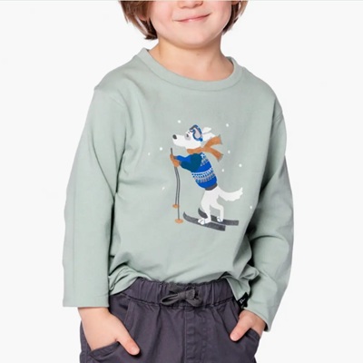 A boy wearing gray pants and a green graphic tee with a white dog skiing 
