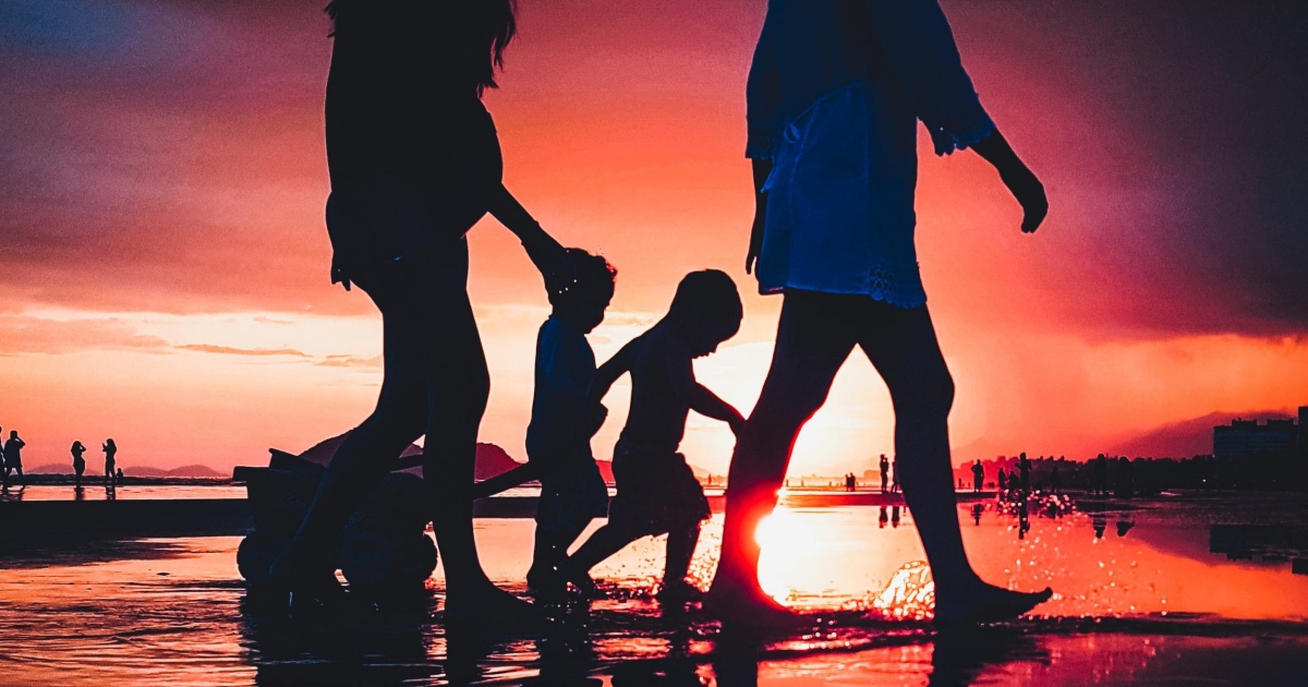 two adults walking on a beach at sunset with two kids under five; one of the adults is pregnant 