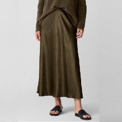 A woman wearing a brown satin skirt, brown sweater, and black slides