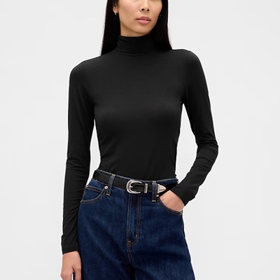 A woman wearing a black long sleeve turtleneck and denim pants with black silver belt