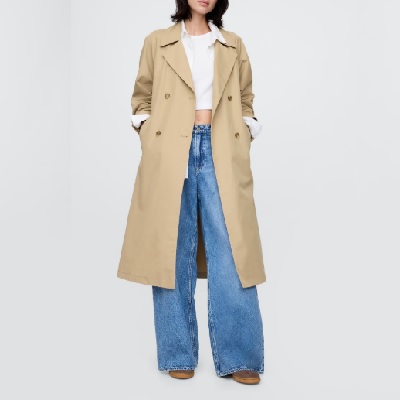 A woman wearing a white top, blue jeans, and khaki trench coat