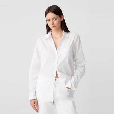 A woman wearing a white, partially-unbuttoned, button-front shirt and white pants
