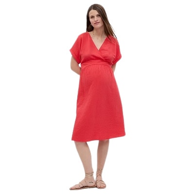 A woman wearing a coral-colored maternity dress and sandals