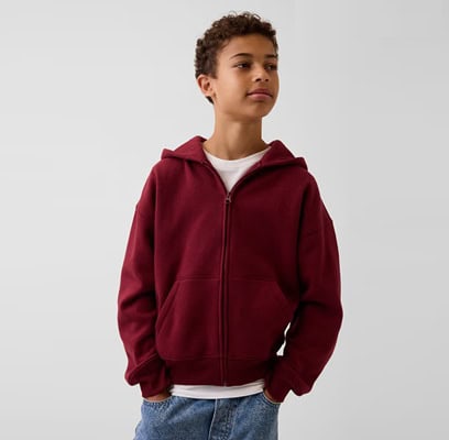A boy wearing a white top, maroon hoodie, and blue jeans