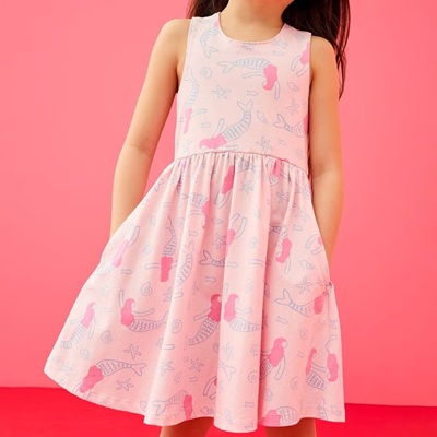 A girl (head and legs cropped out) wearing a light pink dress with a beach and mermaid design