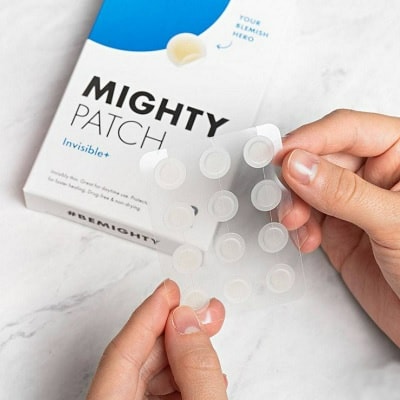 Two hands holding pimple patches in front of the package