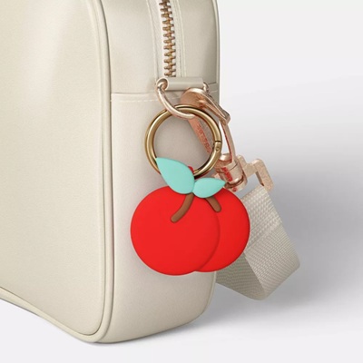 A cream-colored handbag with a cherry-shaped AirTag holder carabiner attached