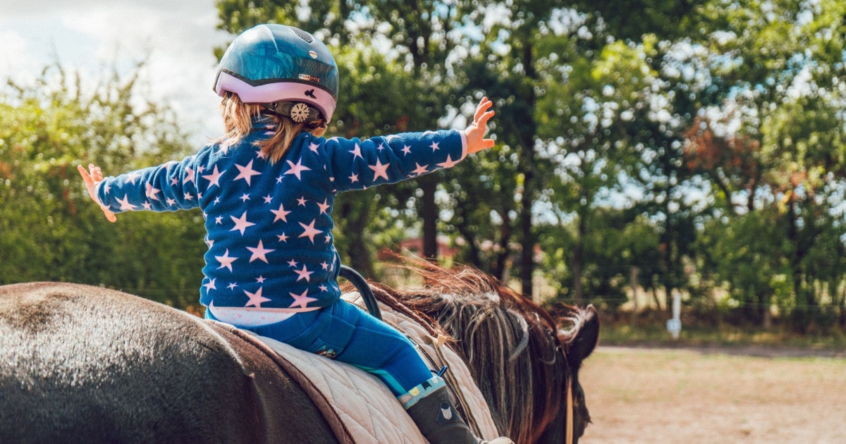 Small girl riding a horse, arms outstretched