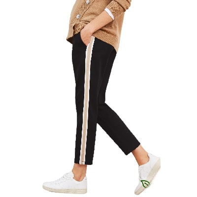 A woman wearing a tan cardigan, black maternity pants with tan and white stripes down the sides, and white sneakers (upper body cropped out)