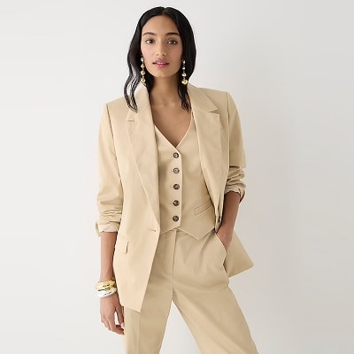 A woman wearing a khaki-colored suit: jacket, vest, and pants, plus gold-tone earrings
