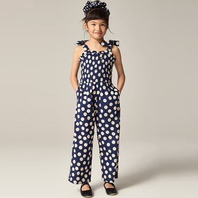 A girl wearing a navy-and-tan dotted jumpsuit and black mary janes