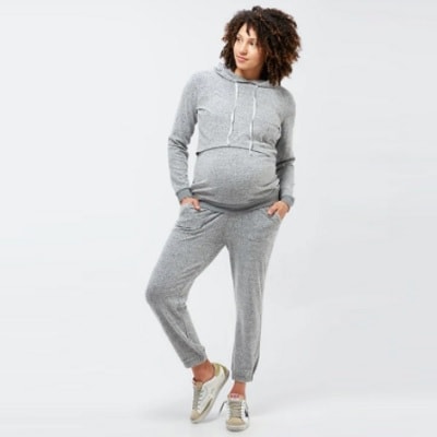 A pregnant woman wearing a gray nursing/maternity hoodie and gray sweatpants with sneakers